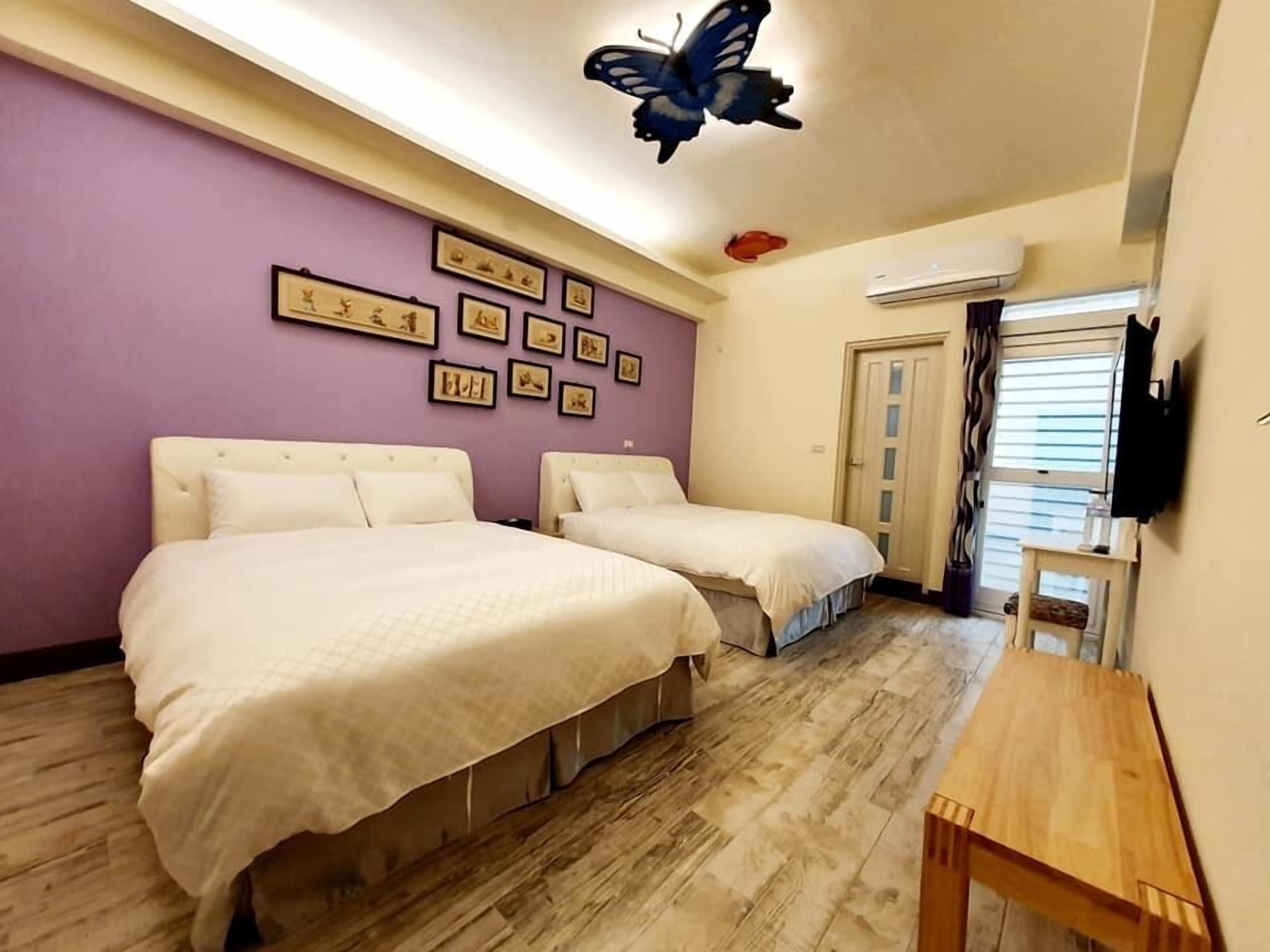 A bedroom with two beds, a wooden table, a TV, and a ceiling butterfly decoration.