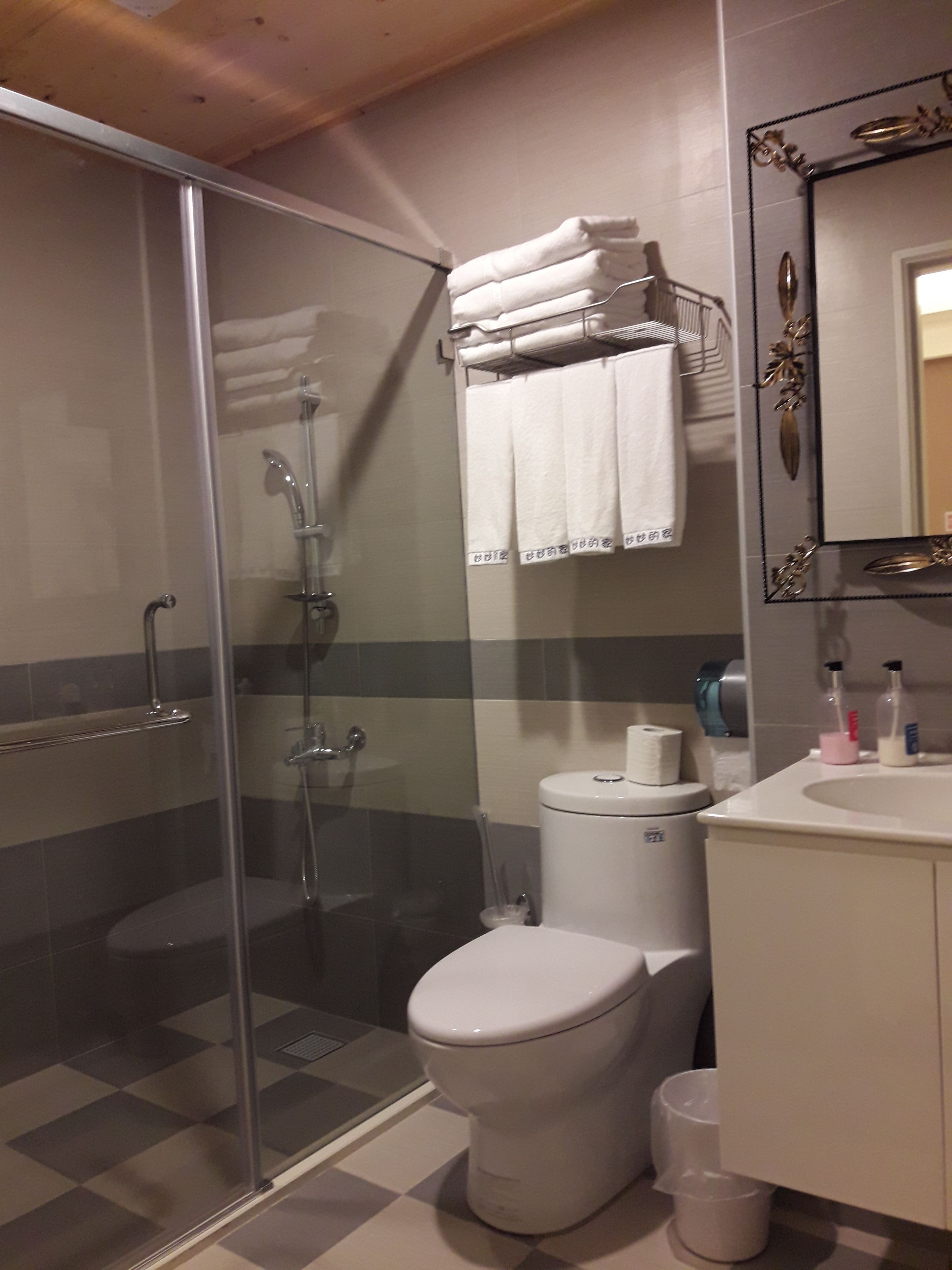 A bathroom with a glass shower enclosure, a toilet, and a sink with toiletries.