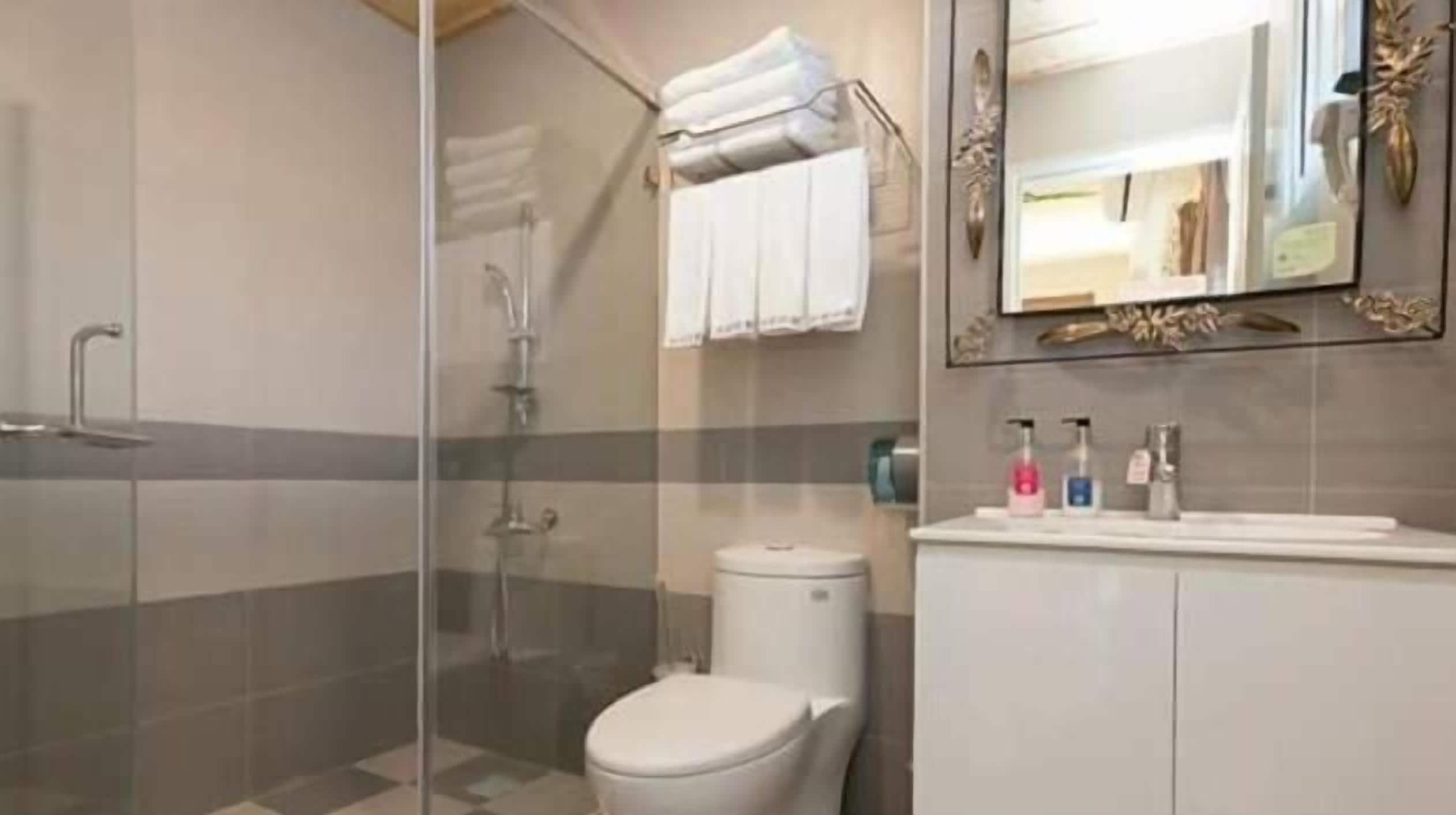 A bathroom with a glass shower enclosure, a toilet, and a sink with soap dispensers.