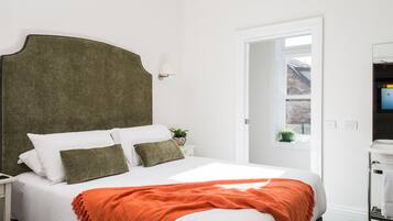 A neatly made bed with white and green bedding, an orange throw blanket, and a green headboard.