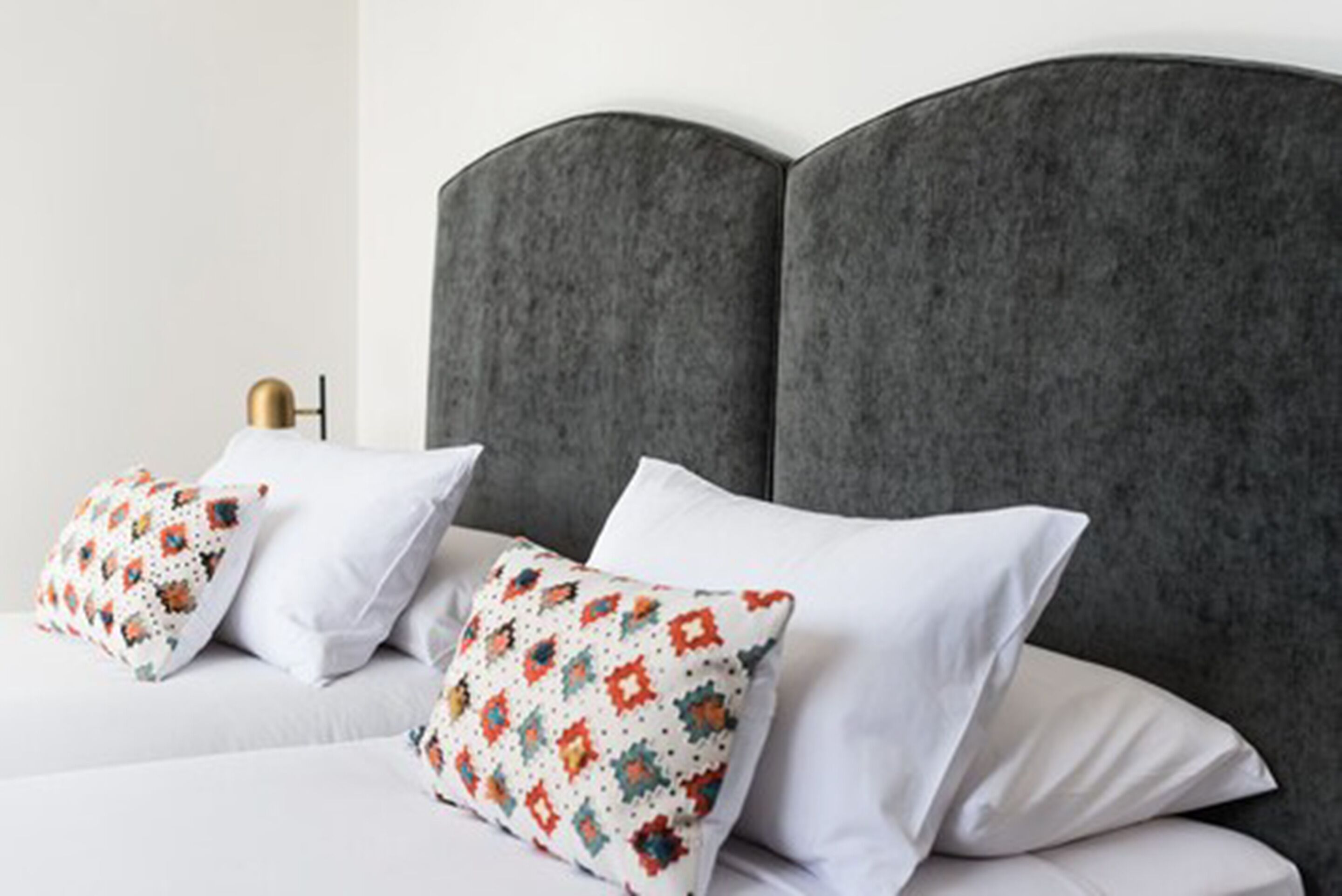 A bed with a grey upholstered headboard, white bedding, and patterned pillows.