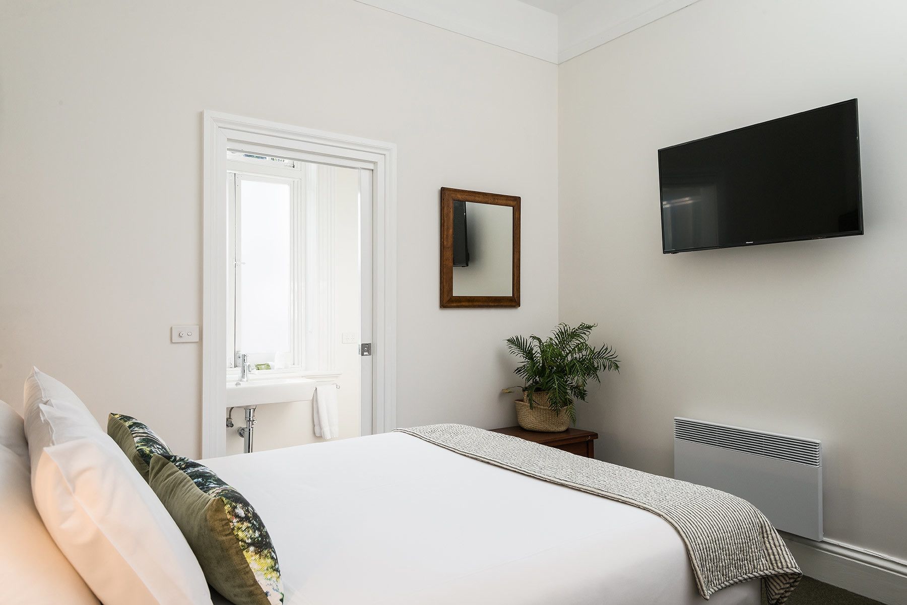 Quarto com cama, televisão, espelho, planta e radiador.