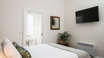 Quarto com cama, televisão, espelho, planta e radiador.