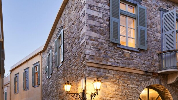 A stone building with a tiled roof, arched windows, and a staircase leading to an upper level. - Guesthouse Lila (Syros)