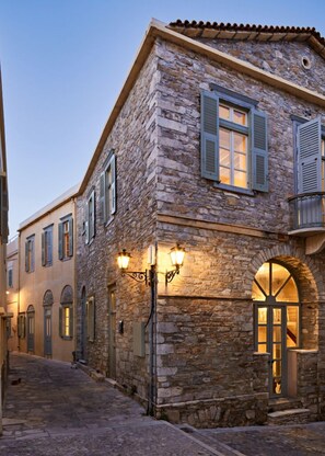 A stone building with a tiled roof, arched windows, and a staircase leading to an upper level. - Guesthouse Lila (Syros)