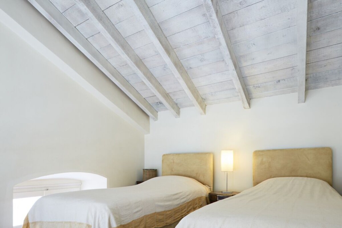 A bedroom with two beds, wooden beams on the ceiling, and bedside lamps.