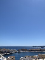 Un pueblo costero con edificios a lo largo del paseo marítimo, un cielo azul despejado y una isla distante.