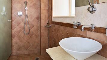 Un baño con lavamanos blanco, ducha con cabezal de ducha de mano y espejo sobre el lavamanos.