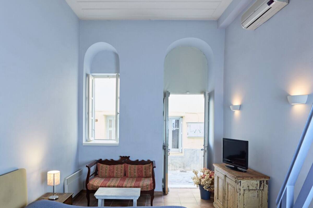 Quarto com cama, sofá, televisão, armário e janela.