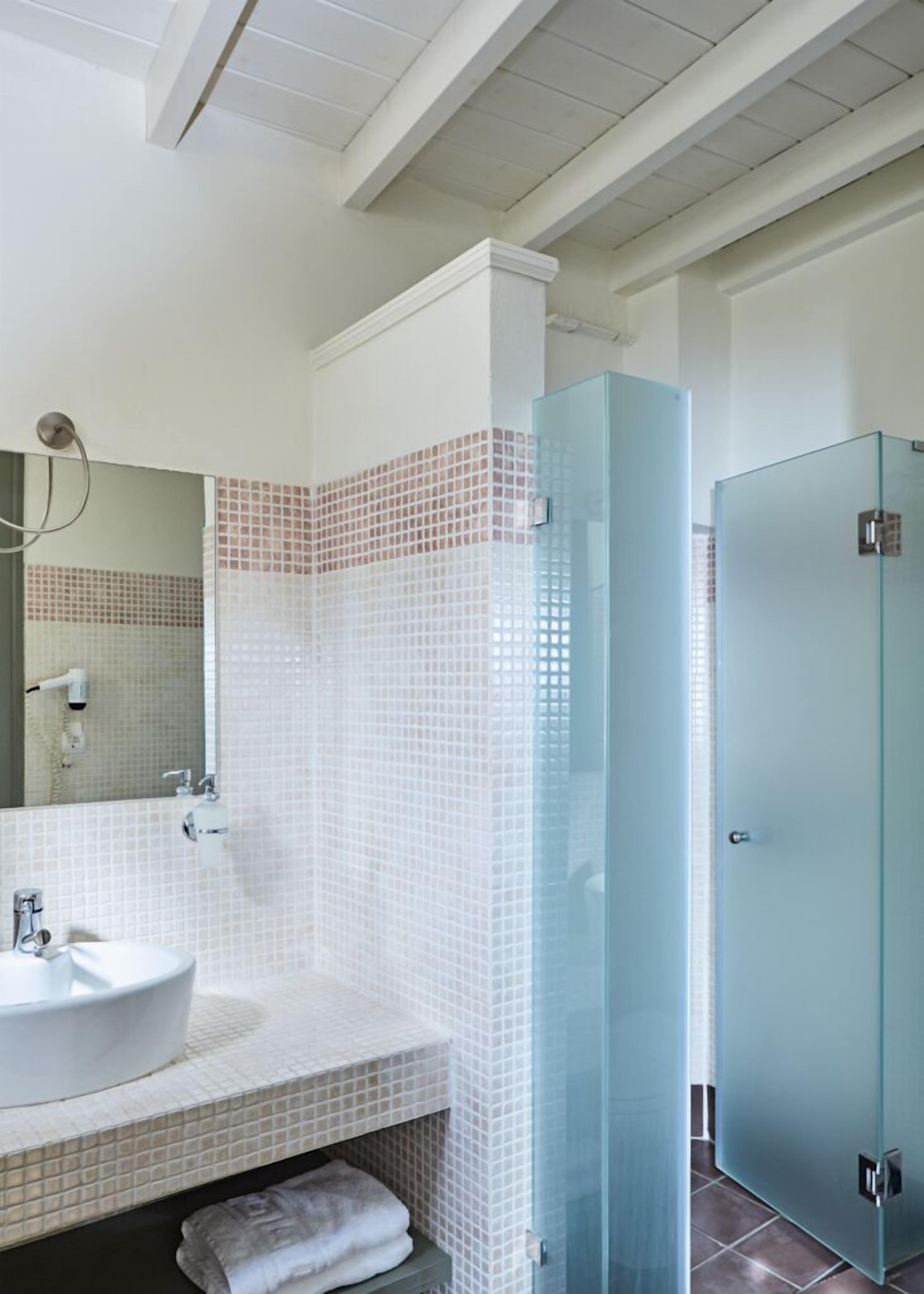 Une salle de bain moderne avec un mur recouvert de carreaux blancs, une douche en verre et un lavabo blanc avec une serviette.
