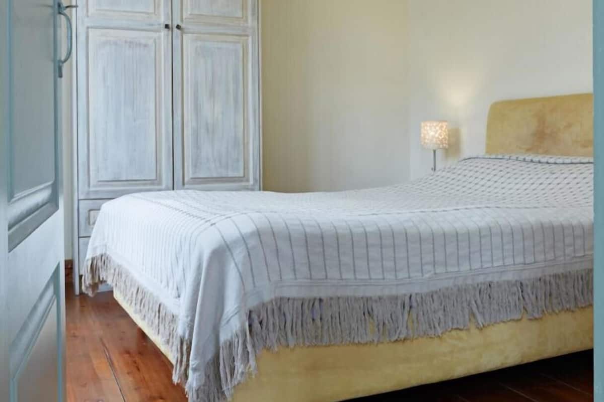 Quarto com cama, guarda-roupa, mesa de cabeceira e luminária no teto.
