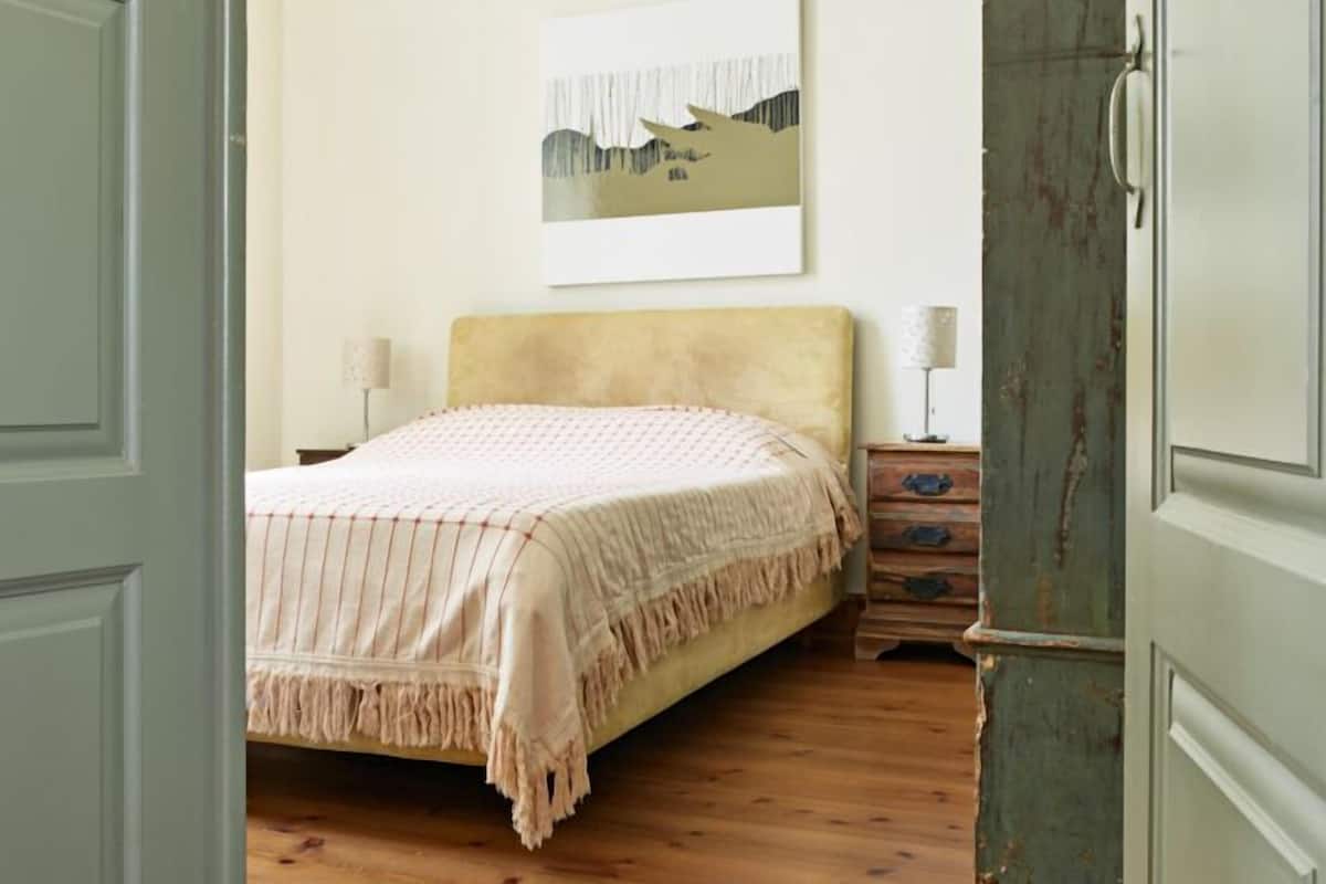 Um quarto com uma cama, uma mesinha de cabeceira, um penteado e um quadro na parede.