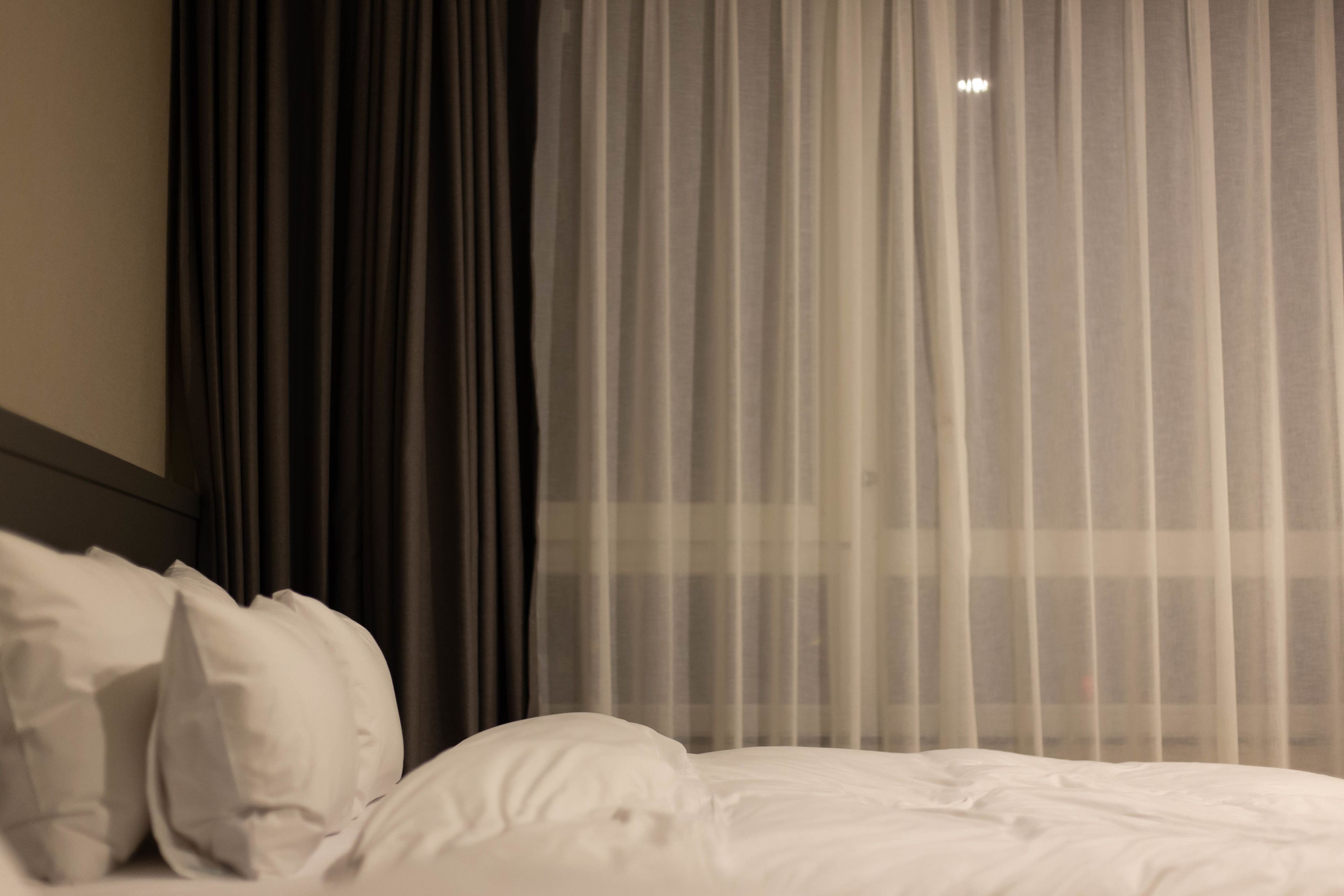 Une chambre d’hôtel avec un lit, du linge de lit blanc et des rideaux en voile.