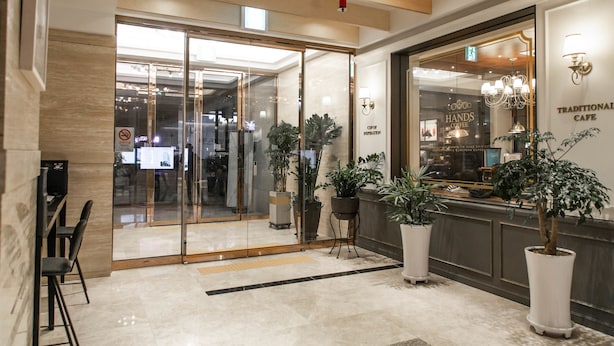 A modern hotel lobby with a glass entrance, potted plants, and a coffee shop named "Traditional Cafe" in the background.