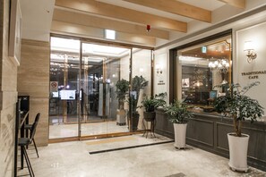 A modern hotel lobby with a glass entrance, potted plants, and a coffee shop named "Traditional Cafe" in the background. - Hotel Daoom (Ulsan)