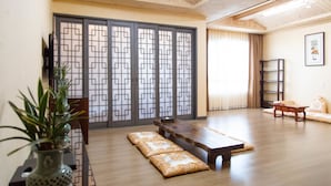 A traditional Japanese-style room with tatami flooring, a low wooden table, cushions, and a sliding door with geometric patterns.