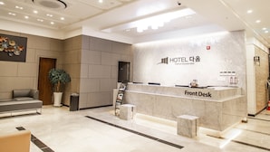 A hotel reception area with a marble front desk, a reception counter, a seating area with a sofa, and a potted plant.