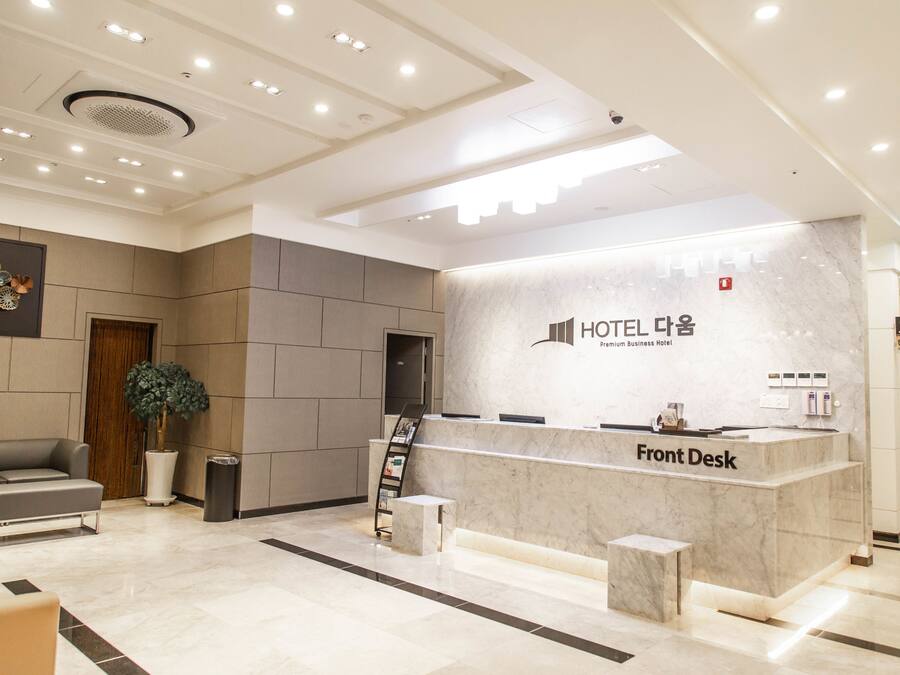 Ein Hotel-Empfangsbereich mit einer Marmor-Rezeption, einer Theke und einer Sitzecke mit Sofa sowie einer Zimmerpflanze.