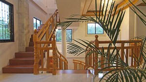 A spacious interior with a wooden staircase, large windows, and a potted plant. - Darcey Residences (Tagbilaran)