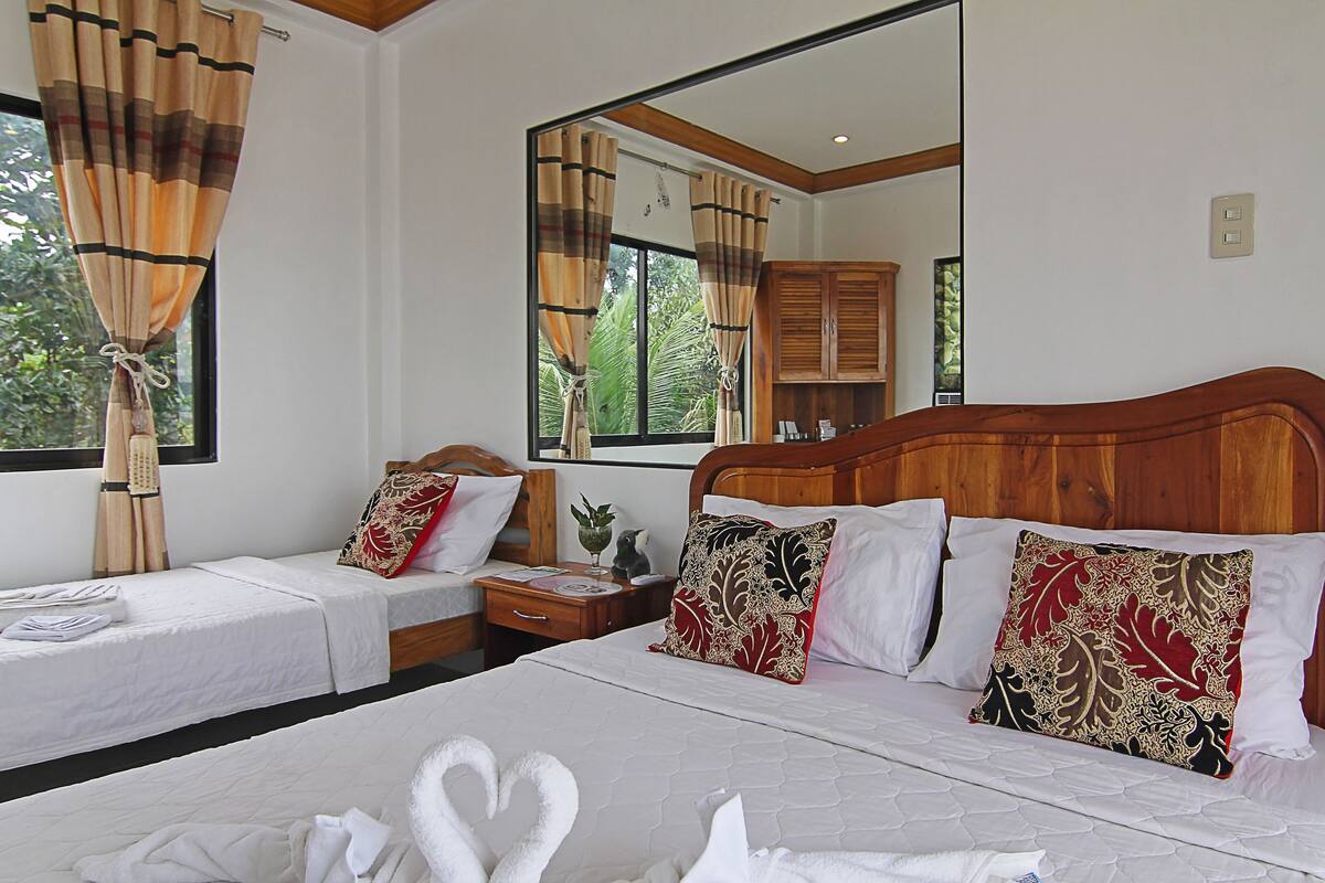 A hotel room with two single beds, a wooden headboard, a nightstand, a mirror, and a window with curtains.
