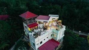 A multi-story building with a red roof, surrounded by dense greenery. - Darcey Residences (Tagbilaran)