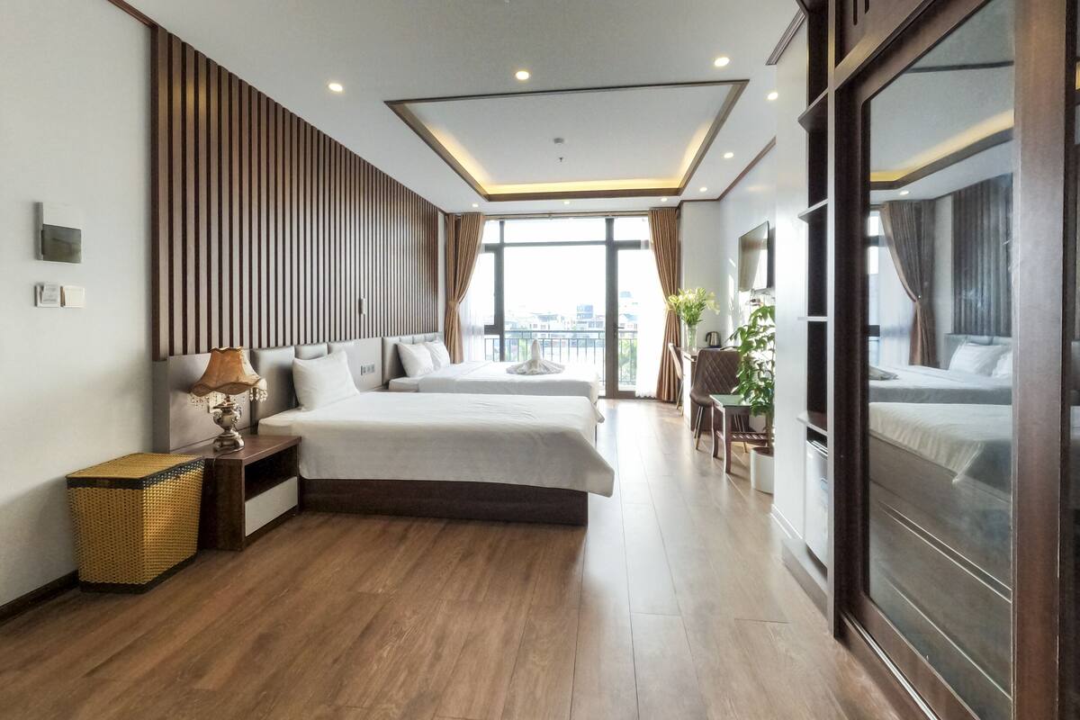 A modern hotel room with two beds, a large window, and a view of the city.