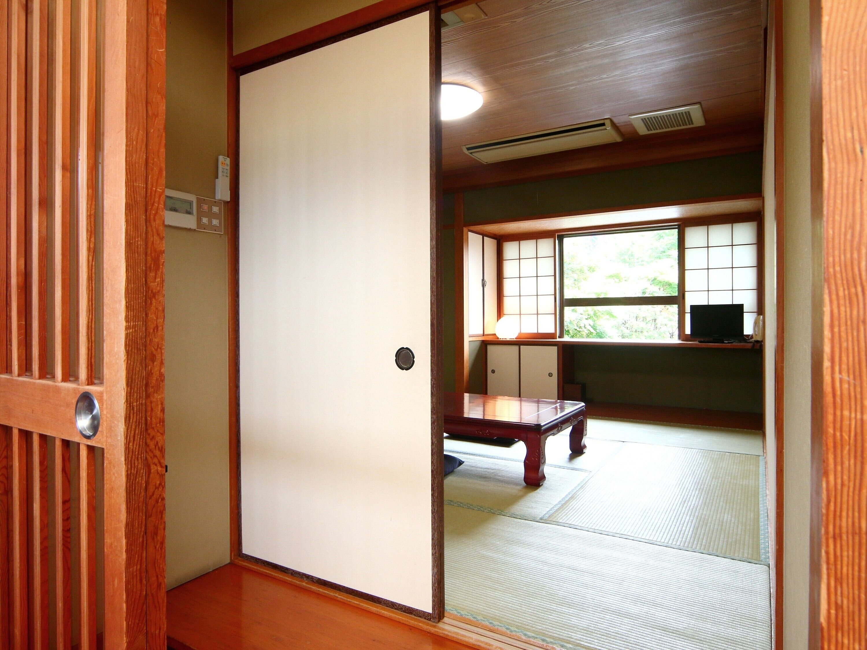 Una habitación japonesa tradicional con suelo de tatami, una puerta corredera shoji y un escritorio de madera bajo con un televisor.