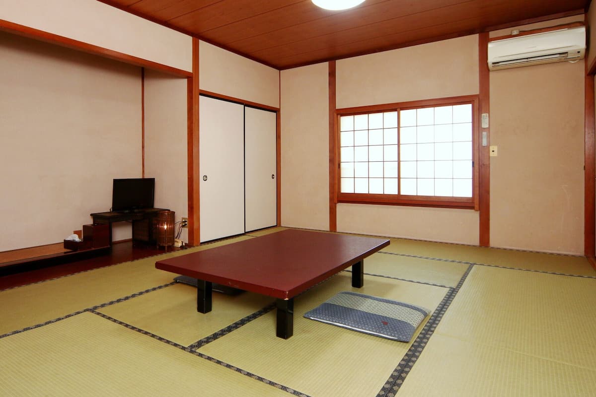 A traditional Japanese room with tatami flooring, a low table, sliding doors, and a window with shoji screens.
