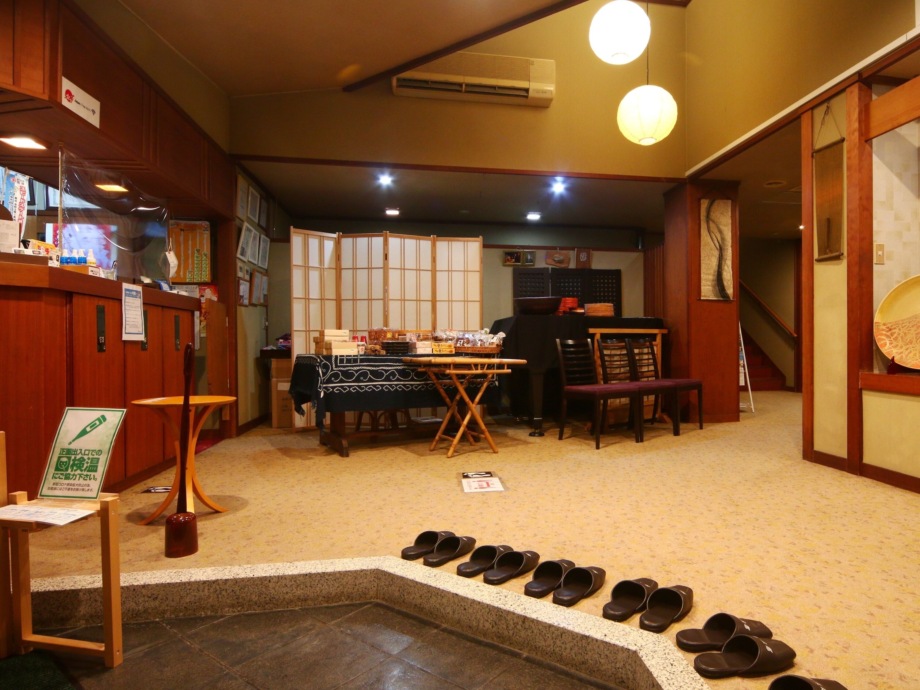 A traditional Japanese room with tatami flooring, a low table with a black tablecloth, wooden chairs, and a set of black slippers lined up on the floor.
