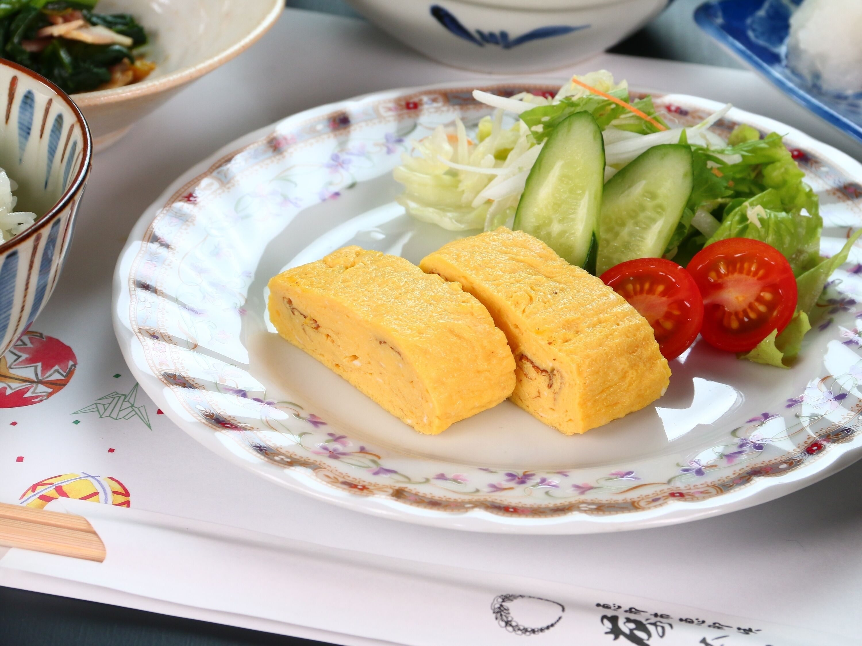 A plate with two pieces of food, a salad, and a bowl in the background.