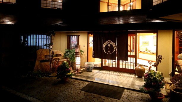 Edifici tradicional d'estil japonès amb entrada empedrada, portes de fusta i plantes en testos.