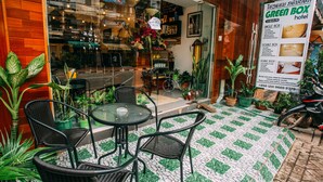 A hotel entrance with wicker furniture, a tiled patio, and a signboard. - Green Box Hotel - Hostel (Vientiane)