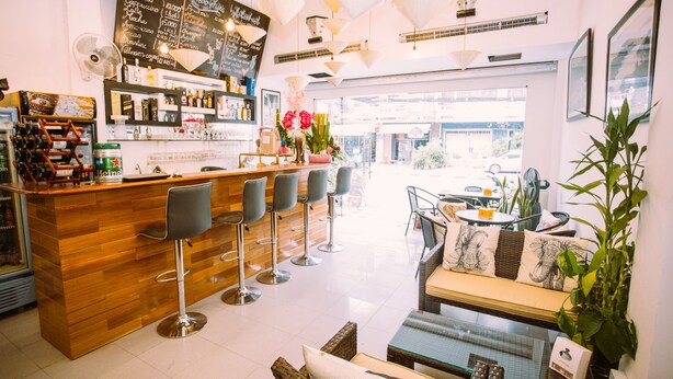 A modern cafe with a wooden counter, bar stools, and a seating area with a sofa and chairs. - Green Box Hotel - Hostel (Vientiane)