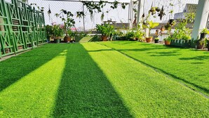 A well-maintained artificial grass lawn with potted plants and a green metal fence. - Green Box Hotel - Hostel (Vientiane)