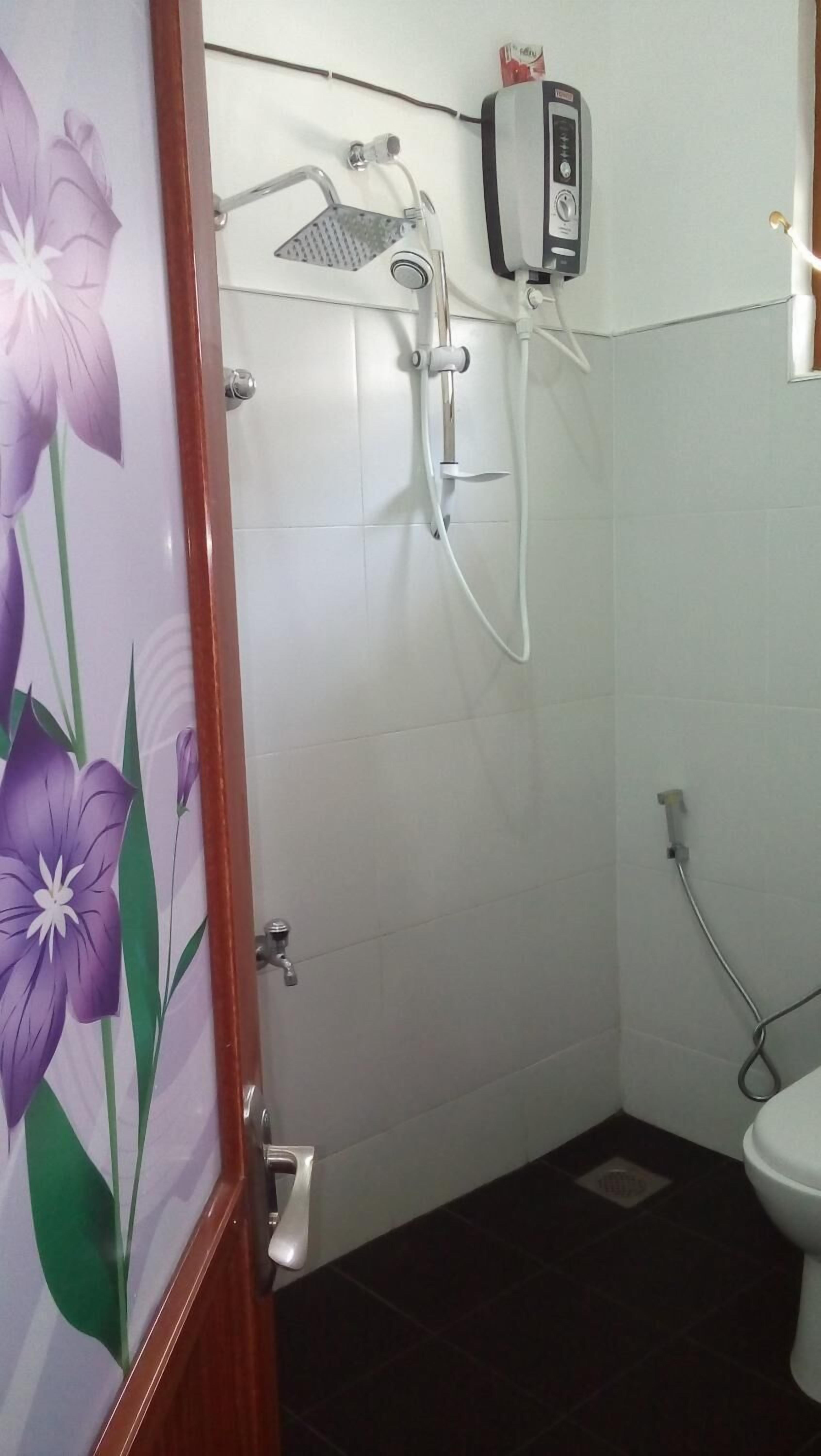 A bathroom with a shower, toilet, and a hand dryer mounted on the wall.