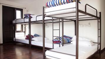 A dormitory room with bunk beds, wooden flooring, and a window.