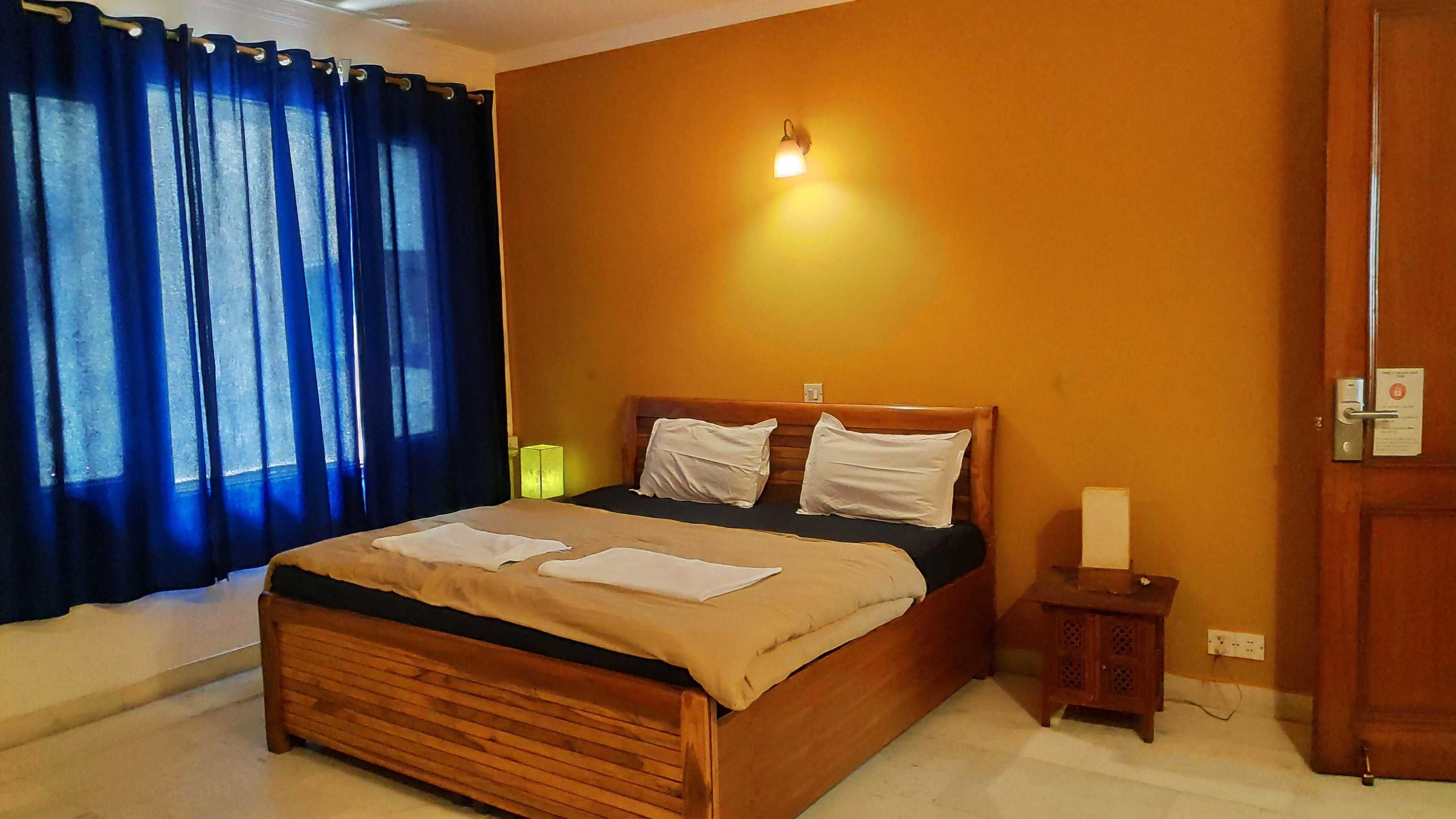 A bedroom with a wooden bed, blue curtains, a wall-mounted light, and a bedside table.