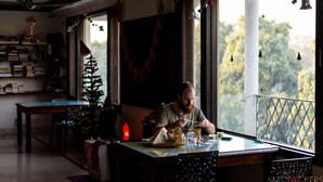 A dining area with a table, chairs, a Christmas tree, and a view of trees outside. - Madpackers Delhi - Hostel (New Delhi)