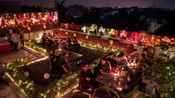 An outdoor dining area with tables and chairs, surrounded by greenery and string lights. - Madpackers Delhi - Hostel (New Delhi)