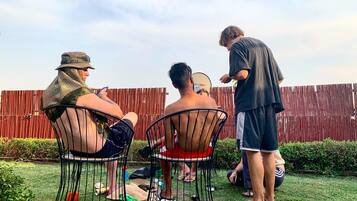 Three people sitting on metal chairs outdoors with a wooden fence in the background.