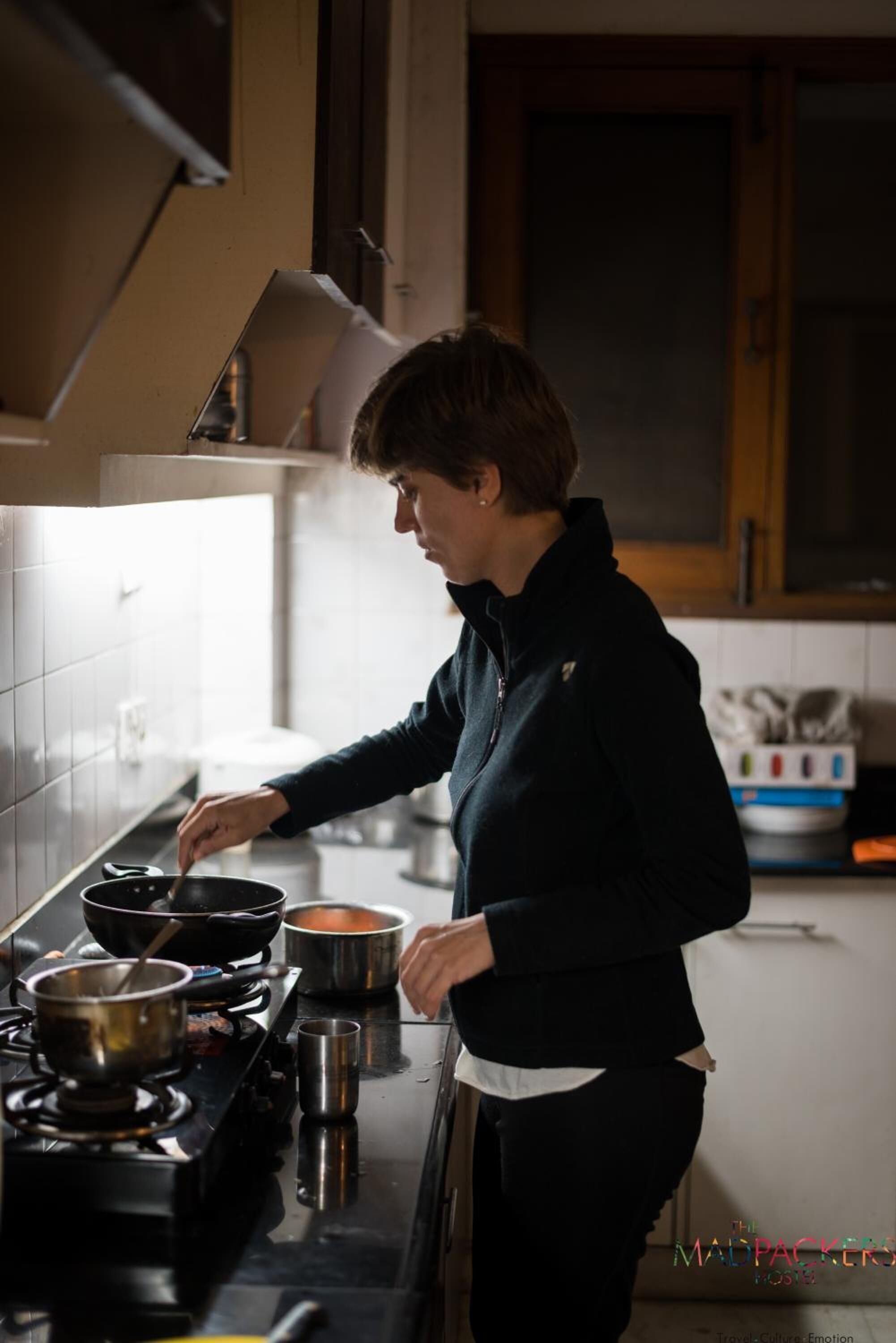 A person cooking in a kitchen with a stove, pots, and a range hood.
