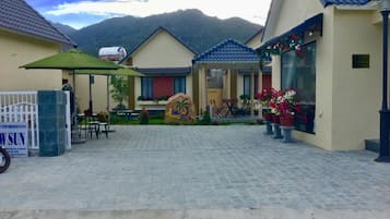 A hotel entrance with a paved driveway, outdoor seating, and a mountain backdrop.