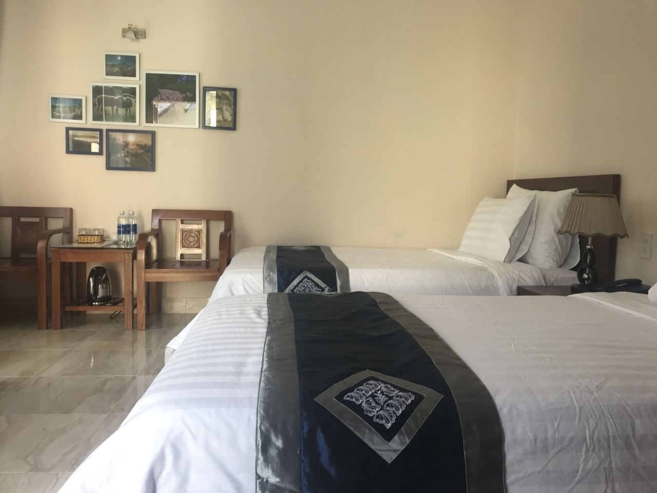 Ein Hotelzimmer mit zwei Betten, einem Holztisch, einem Stuhl und einer Wand mit gerahmten Bildern.
