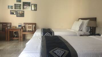 Ein Hotelzimmer mit zwei Betten, einem Holztisch, einem Stuhl und einer Wand mit gerahmten Bildern.