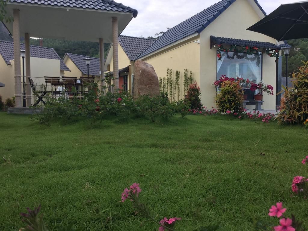 A residential area with a covered patio, a house with a tiled roof, and a garden with pink flowers.