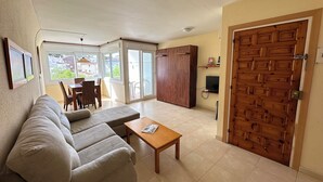 Ein Wohnzimmer mit einer Couch, einem Holztisch und einer Schiebetür, die auf einen Balkon führt.
