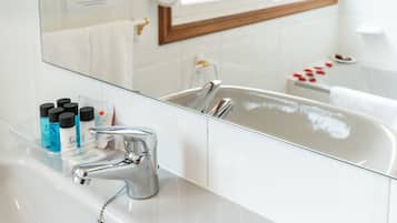 A bathroom with a white sink, a mirror, and a bathtub. There are toiletries on the sink and a towel rack above the bathtub.