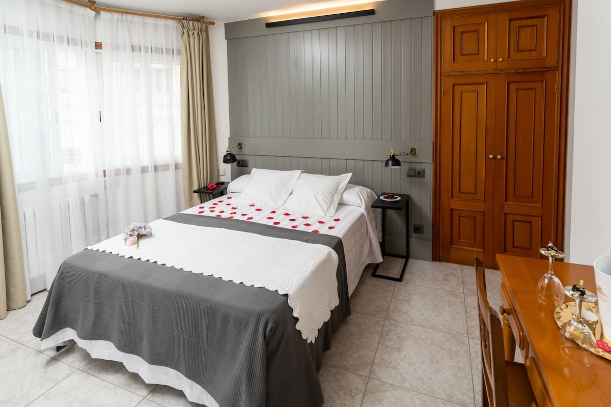 Un lit bien fait, recouvert d’une couvre-lit blanche et grise, une table de chevet avec une lampe et une armoire en bois.