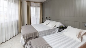 A hotel room with two beds, a nightstand, a lamp, and a window with curtains. - Hotel Panadeiramar (Sanxenxo)