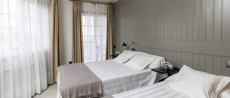 Habitación de hotel con dos camas, una mesita de noche, una lámpara y una ventana con cortinas.